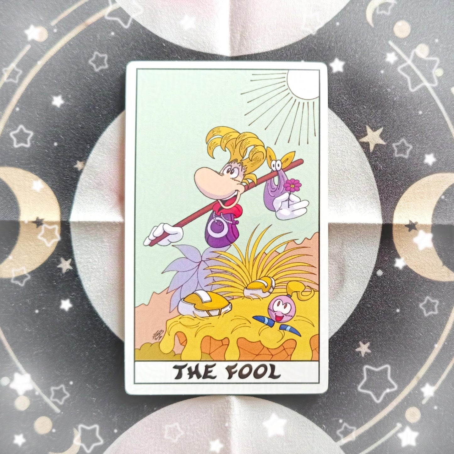Photo of a vinyl sticker which is of The Fool tarot card but it's Rayman and an Electoon.