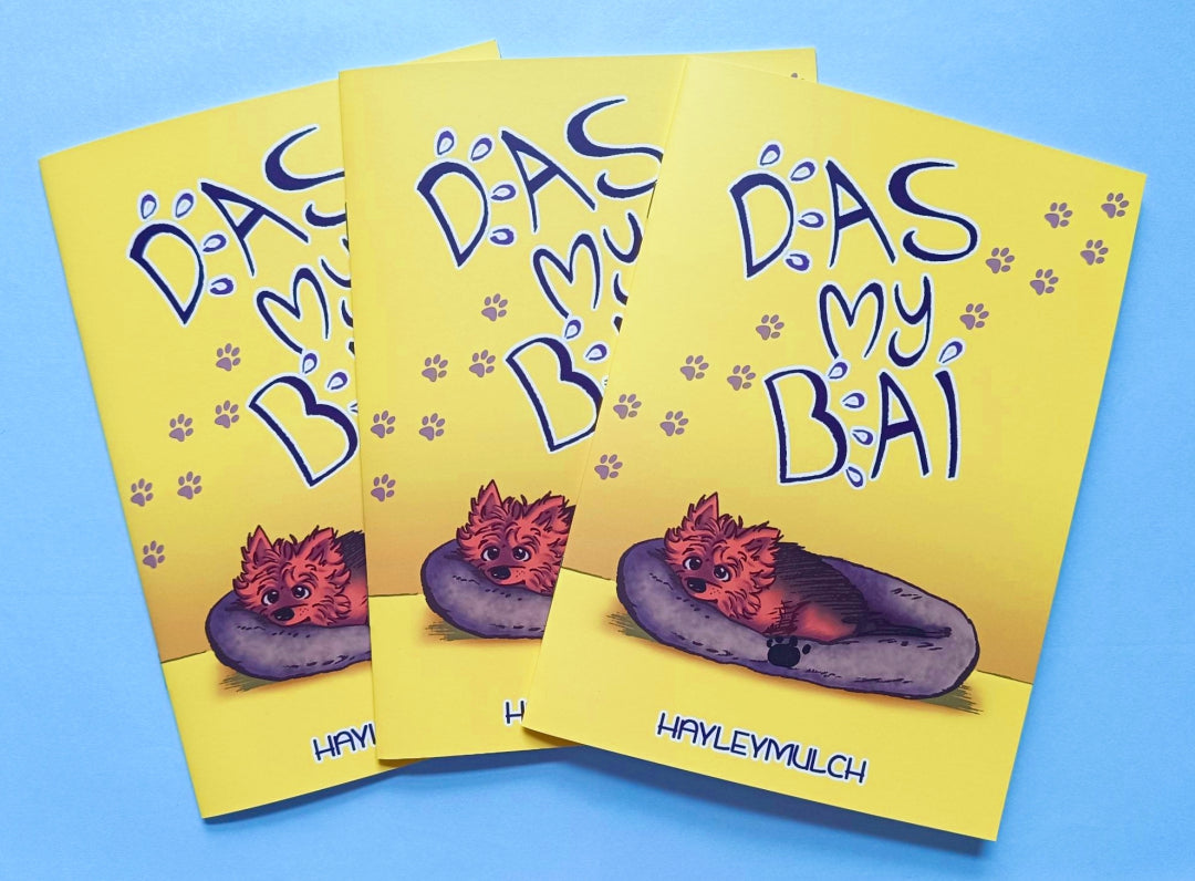 Three copies of the comic Das My Bai. It's a mostly yellow book cover with a dog in a bed and the title of the book written in big text.