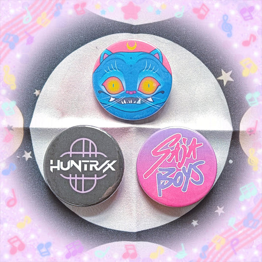 Photo of 3 button badges, each with a separate design from the movie about Demon Hunters and the main characters also sing KPop songs. One has the face of the tiger and the others are the logos of the 2 main KPop bands in the movie.