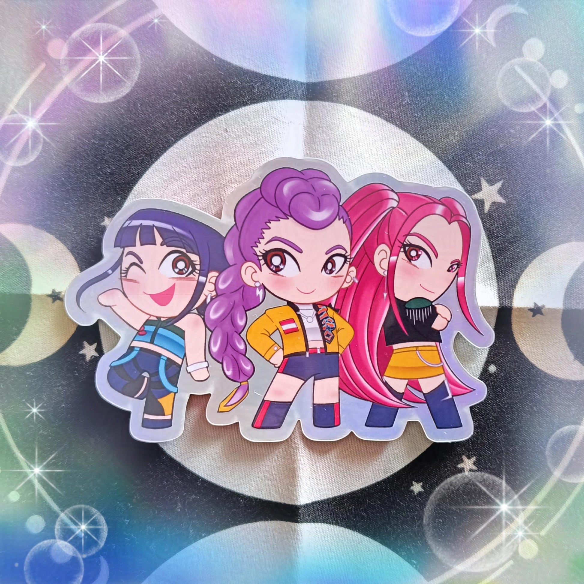 Photo of a holographic sticker featuring the main women characters in chibi style from the movie about Demon Hunters and they're also in a KPop band.