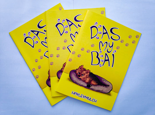 Three copies of the comic Das My Bai placed against a light blue background. It's a mostly yellow book cover with a dog in a bed and the title of the book written in big text.