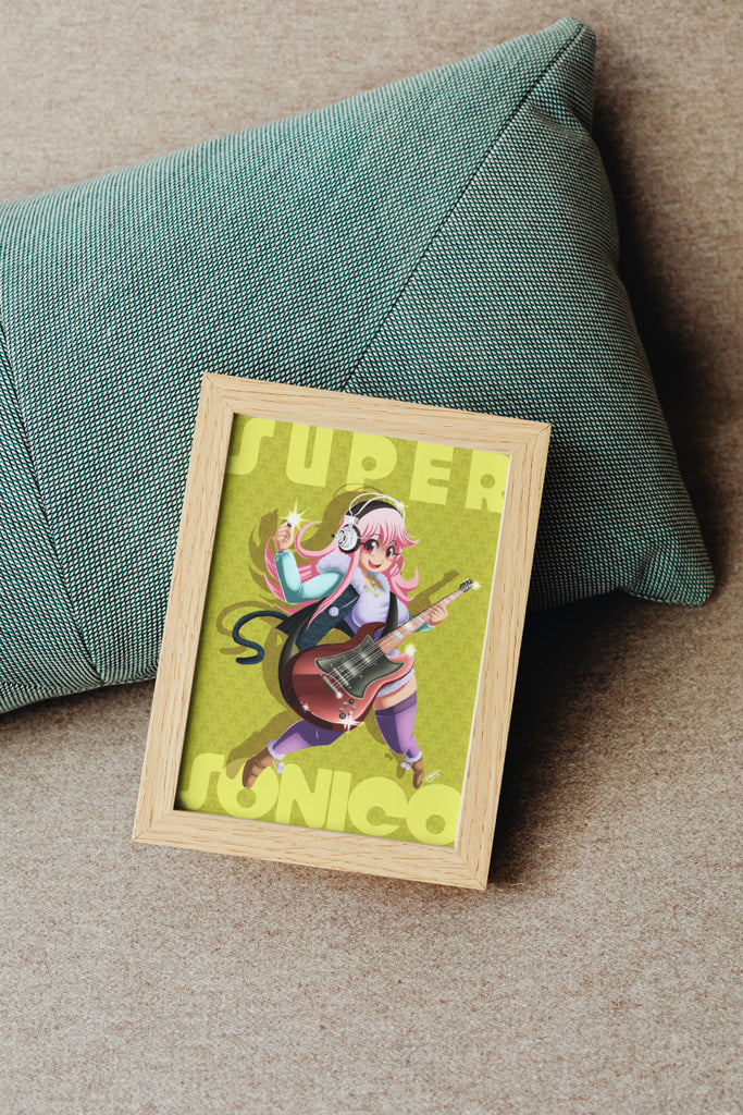 The aforementioned Super Sonico illustration in a mock up wooden frame, placed against a sage green pillow on a beige couch.