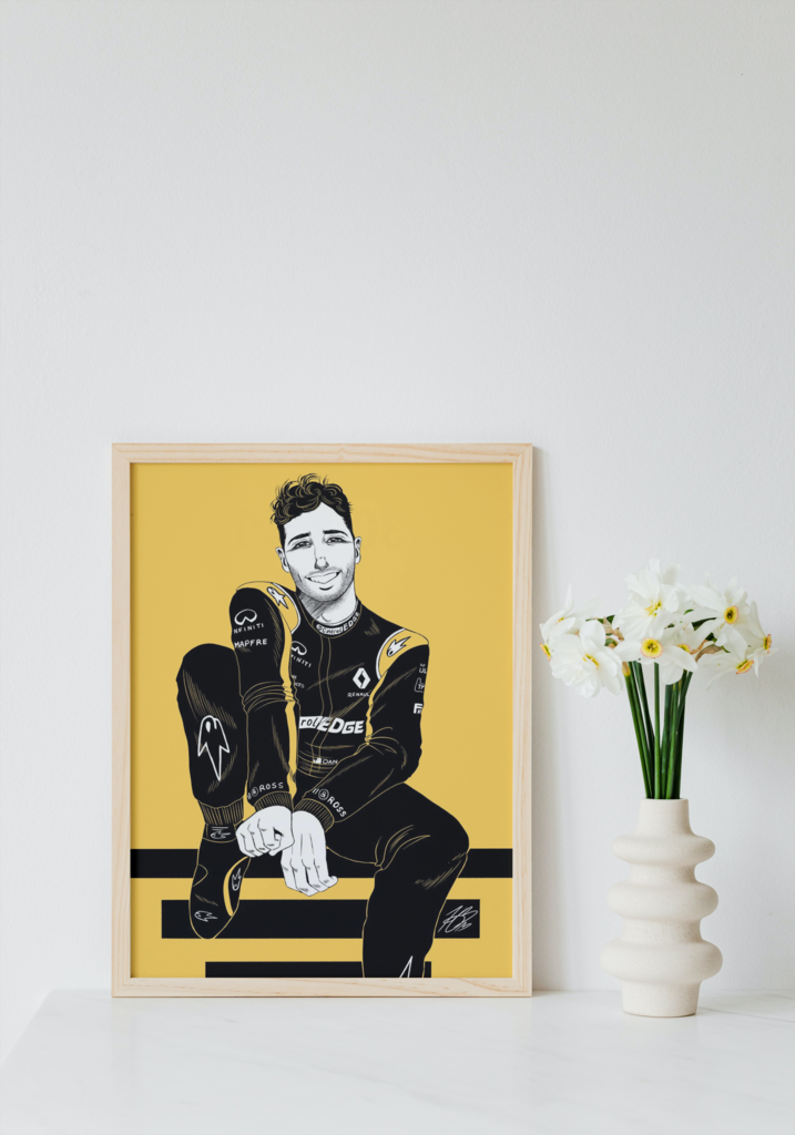 The aforementioned illustration of Daniel Ricciardo displayed in a mock-up frame for real life reference. It's in a white wooden frame, leaning against a white wall and placed on a white table. A white vase is to the right of the frame and houses white and yellow daffodils.